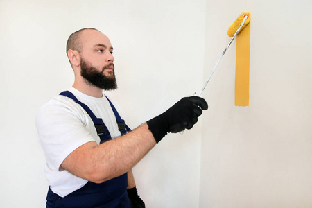 专业油漆工在施工现场用油漆辊刷涂黄色墙面.家居装修概念.照片