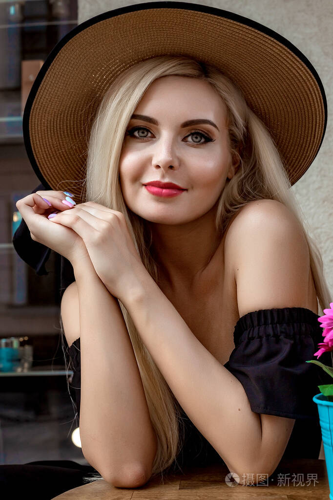 一位优雅女士的高级时装肖像戴着优雅的草帽和礼服坐在咖啡厅的桌子旁