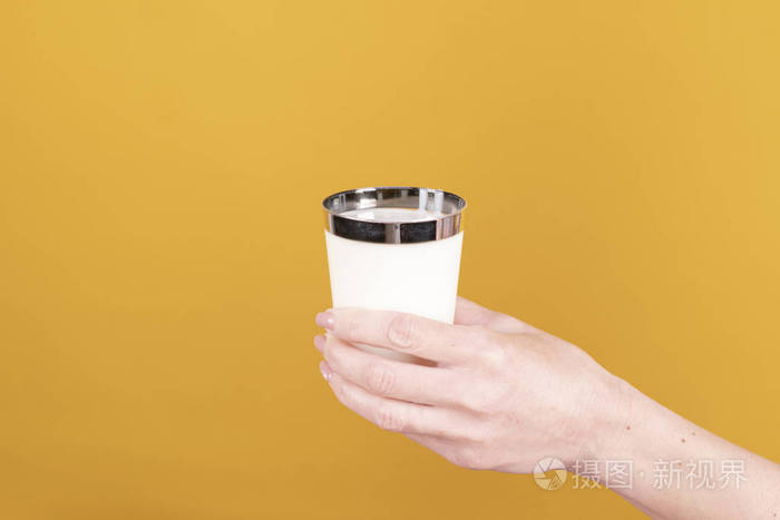 女人的手拿着一杯牛奶背景是黄色
