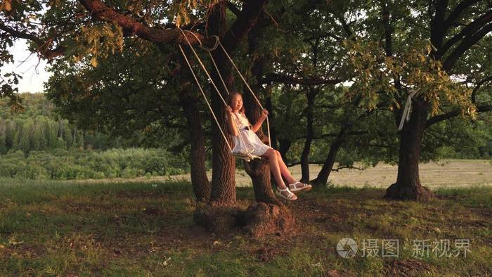 小女孩在阳光下在树下荡秋千和孩子们玩耍特写镜头大自然中的家庭乐趣