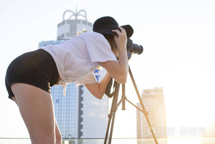 一个女摄影师拿着相机和一个三脚架在城市的背景上，她在日落时拍照，一个女人拍摄一段视频