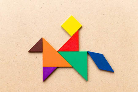 木头人游戏彩色七巧板拼图在人骑马形状的木头背景上照片