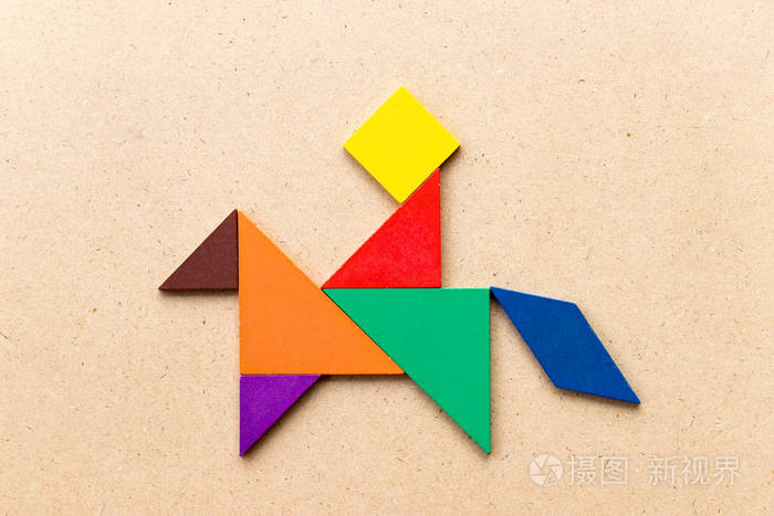 彩色七巧板拼图在人骑马形状的木头背景上