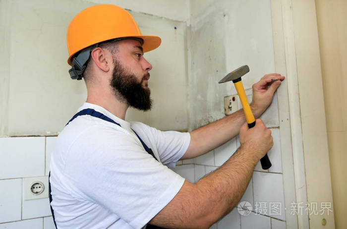 施工现场,建筑工人用黄锤敲打并钉入厨房门的木墙上.公寓装修概念.