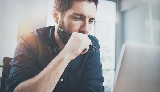 沉思的男人使用当代的便携式电脑在办公室.变模糊后台