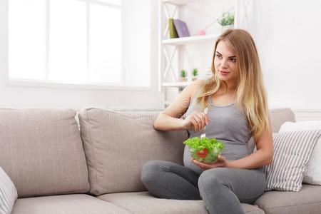 年幼的怀孕的女人吃新鲜的绿色的沙拉