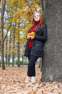 年幼的女人台在近处树采用秋公园,黄色的树叶
