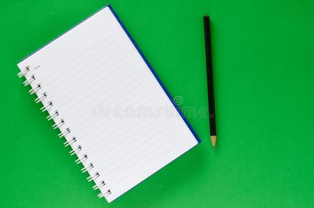 白色的笔记书和黑的铅笔向绿色的颜色背景和