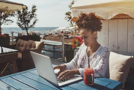 黑的女孩使用便携式电脑采用咖啡馆在近处海