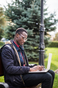 年幼的非洲的男人和便携式电脑一次向一木制的长凳一nd打字