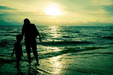 母亲和儿子轮廓日落向海滩