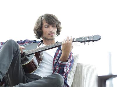 英俊的男人演奏向指已提到的人吉他向指已提到的人长沙发椅在家