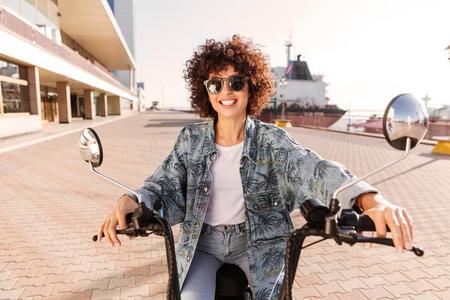 幸福的有卷发的女人采用太阳镜乘向现代的摩托车