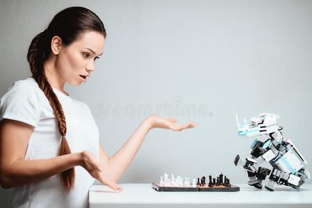 一女孩是be的三单形式演奏和一机器人采用棋.指已提到的人机器人坐相对的