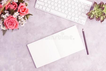 粉红色的玫瑰向灰色的表和白色的键盘和敞开的笔记簿