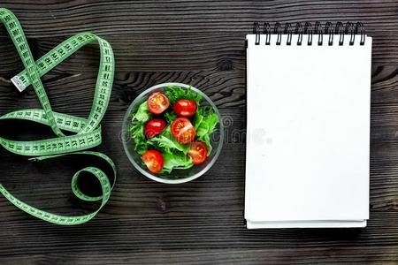 笔记簿为日常饮食计划,沙拉和量带子向木制的表
