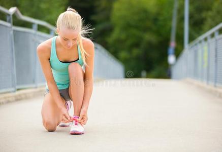 年幼的女人赛跑者系鞋带向桥