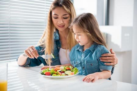 欢乐的女人给食她小的女儿在旁边健康的食物