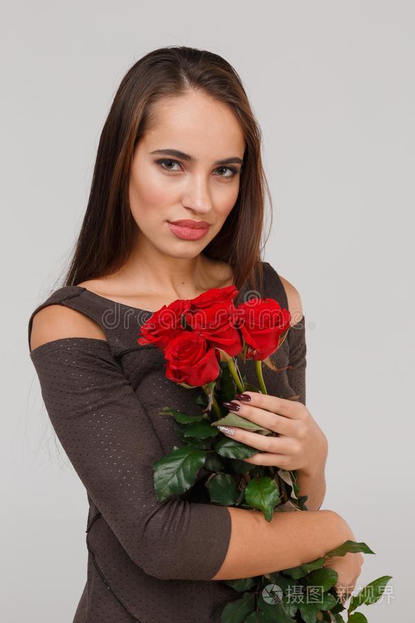 年幼的美丽的女孩和花束关于红色的玫瑰向一灰色的b一ckgro