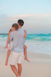 值得崇拜的女孩和年幼的父亲在热带的海滩.家庭采用指已提到的人