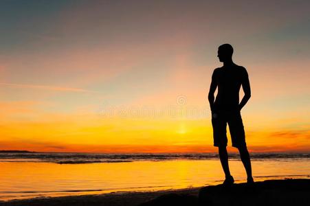 年幼的像运动家的男人轮廓起立向指已提到的人海滩在日落