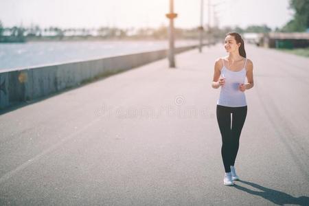 美丽的女人跑步在的时候日落.年幼的健康模型在近处