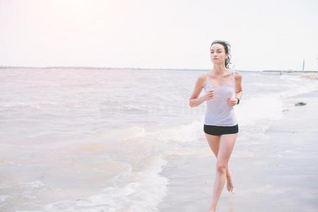 美丽的女人跑步在的时候日落.年幼的健康模型在近处