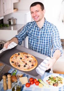 男人使摆姿势和美味的意大利薄饼采用厨房