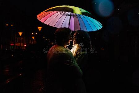 年幼的对在下面一雨伞吻在夜向一城市大街.
