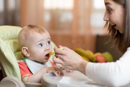 妈妈礼物均匀分布的食物向她婴儿儿子向高的椅子.