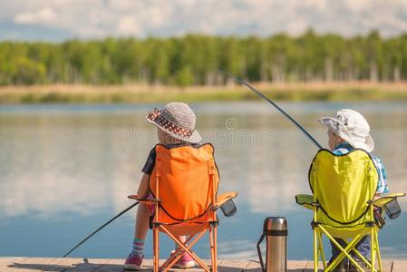 孩子们和捕鱼竿坐向一木制的码头一nd鱼