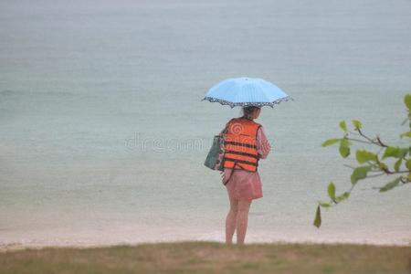 旅行者和雨伞和雨衣或生活短上衣向指已提到的人海滩