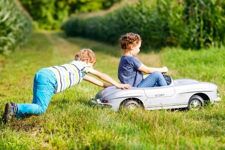 两个幸福的孩子们演奏和大的老的玩具汽车采用夏花园