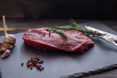 生的牛肉牛排和迷迭香,胡椒粉加里克向黑暗的st向e,餐叉照片