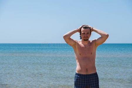 英俊的男人使摆姿势向海滩,肖像.手采用头发.