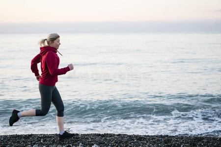 成熟的女人赛跑者跑步向日出海滨.健康的生活方式