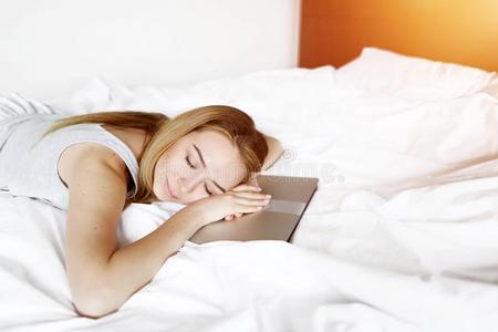 女人疲倦的关于使工作睡在便携式电脑床和白色的亚麻布在家