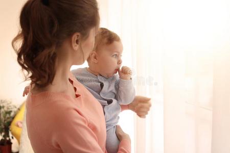 年幼的母亲和她漂亮的小的婴儿在近处窗