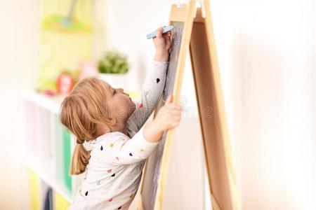 幸福的小的女孩绘画向粉笔板在家
