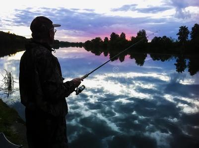 轮廓关于渔夫和捕鱼杆向湖采用日出.照片