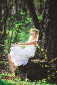 美丽的女人采用白色的衣服坐在旁边树绿色的森林.