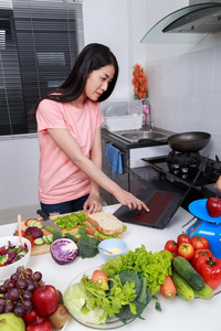 女人烹饪术和有样子的和便携式电脑采用厨房房间