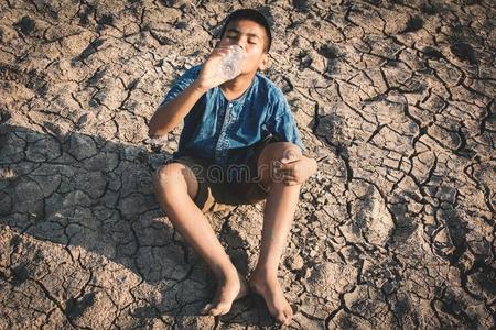 悲哀的男孩喝饮料水向破裂地面