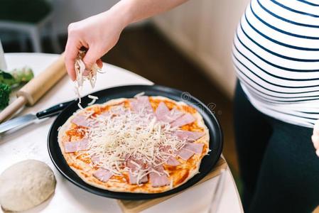 怀孕的女人烹饪术,放置奶酪和意大利干酪向意大利薄饼
