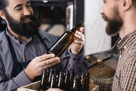 两个成熟的有胡须的人检查质量关于啤酒瓶子玻璃在酿造