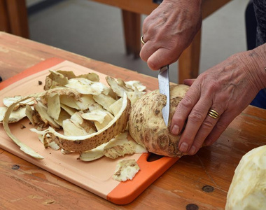 年长的女性的手将切开芹菜和一厨房刀向一木制的英语字母表的第20个字母