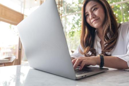 一美丽的一sian女人使用和打字向便携式电脑采用咖啡馆