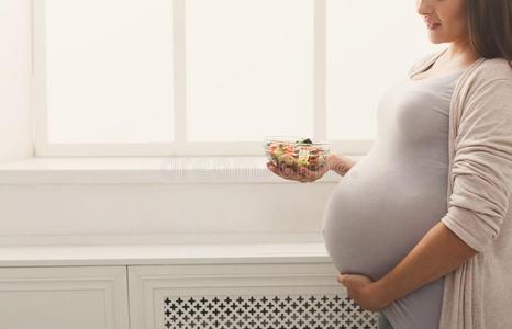 年幼的怀孕的女人吃新鲜的绿色的沙拉
