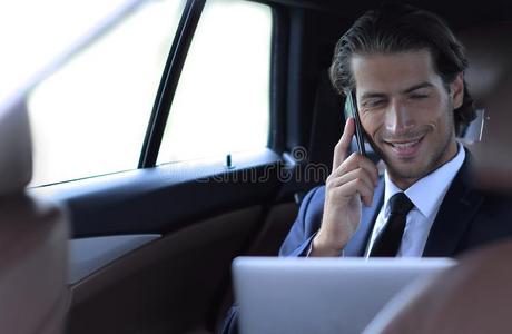 英俊的商人使用可移动的电话采用汽车.