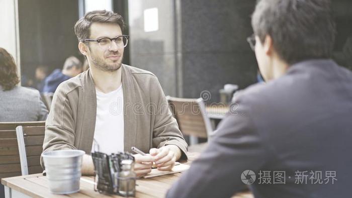 一男人采用眼镜talk采用glisten采用g向他的朋友在咖啡馆外